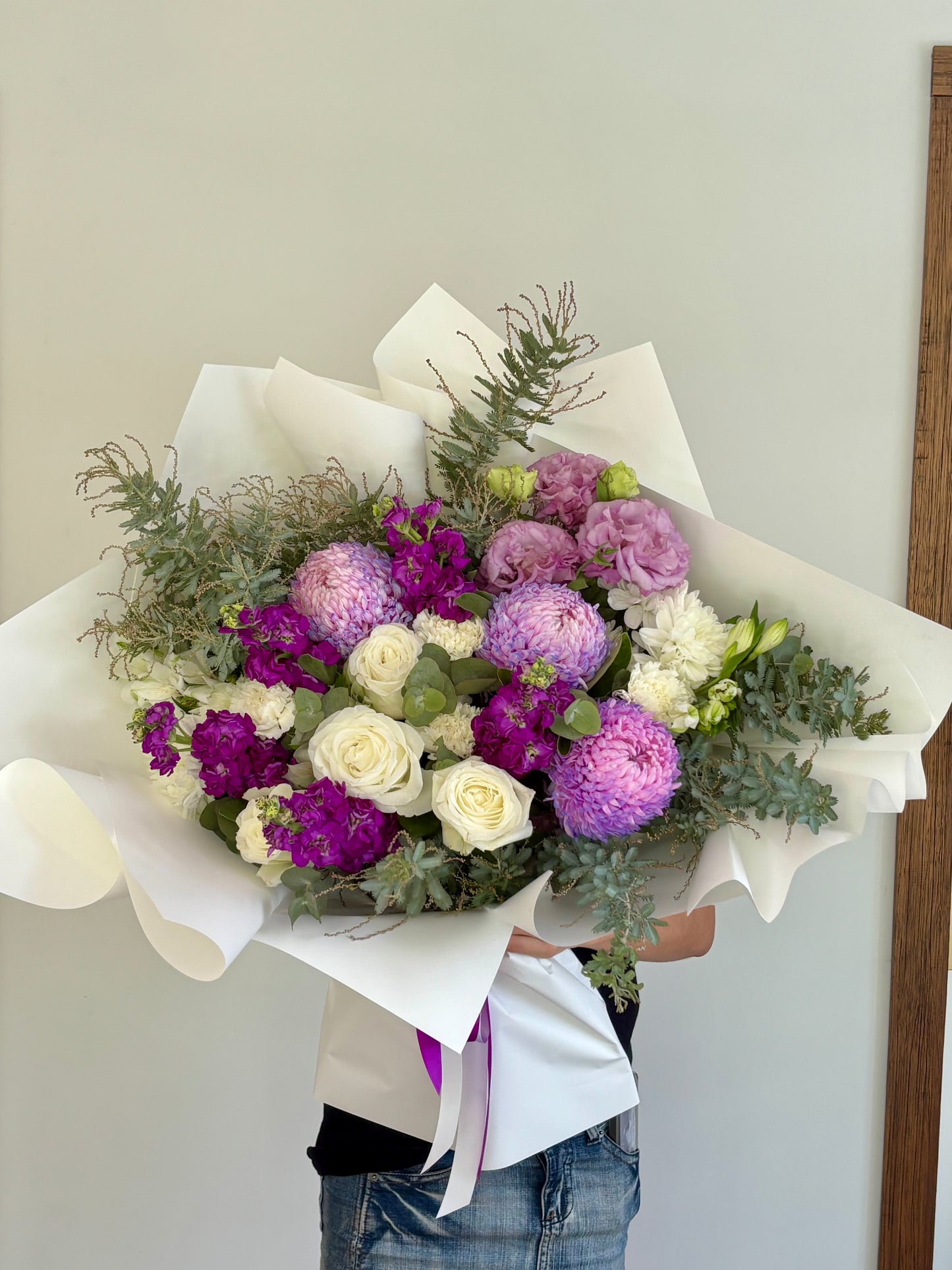 Large romantic bouquet with purple chrysanthemums, lilac lisianthus, white spray roses and eucalyptus, wrapped in white paper with magenta ribbon