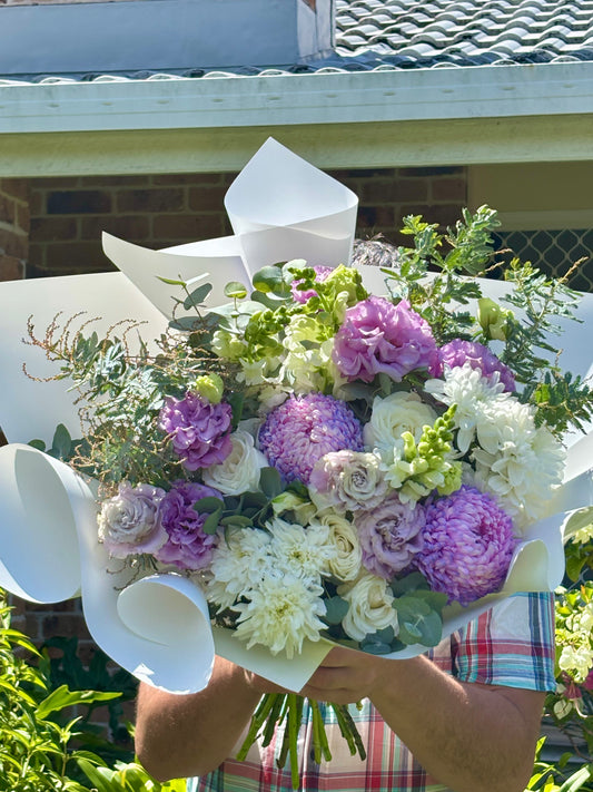 Large romantic bouquet with purple chrysanthemums, lilac lisianthus, white spray roses and eucalyptus, wrapped in white paper with magenta ribbon