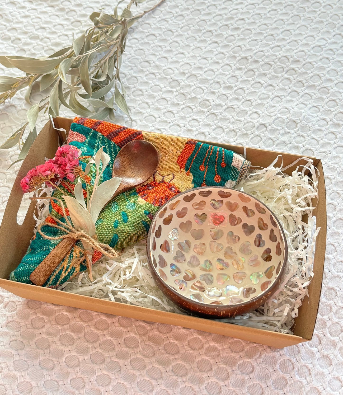 Gift set with a wooden bowl, spoon, and decorative items in a box on a textured surface.