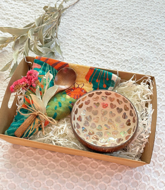 Gift set with a wooden bowl, spoon, and decorative items in a box on a textured surface.