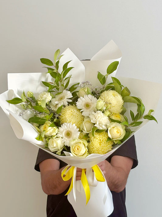 Bouquet of yellow and white flowers wrapped in white paper with a yellow ribbon 